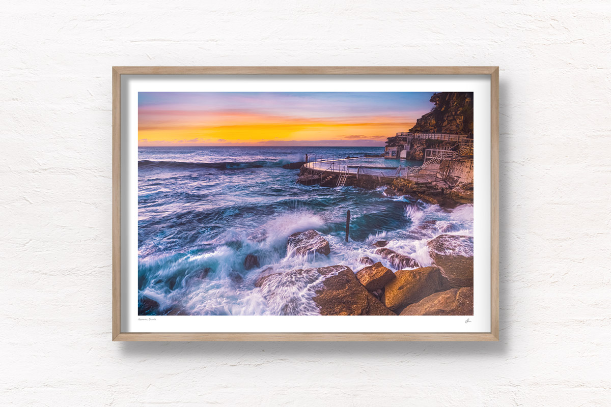 Long exposure of a swimmer stands on the edge of Bronte rockpool watching the sun rise over the horizon.