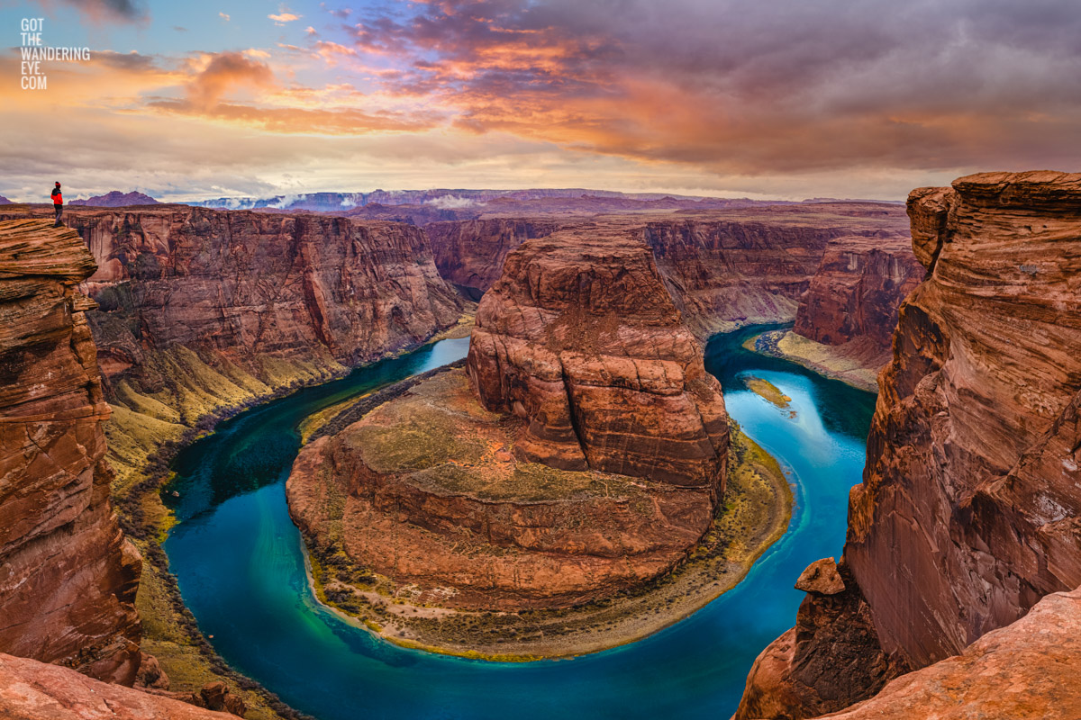 Man observing the Colorado river curving around the lookout at Horseshoe Bend, Arizona during a stormy sunrise.