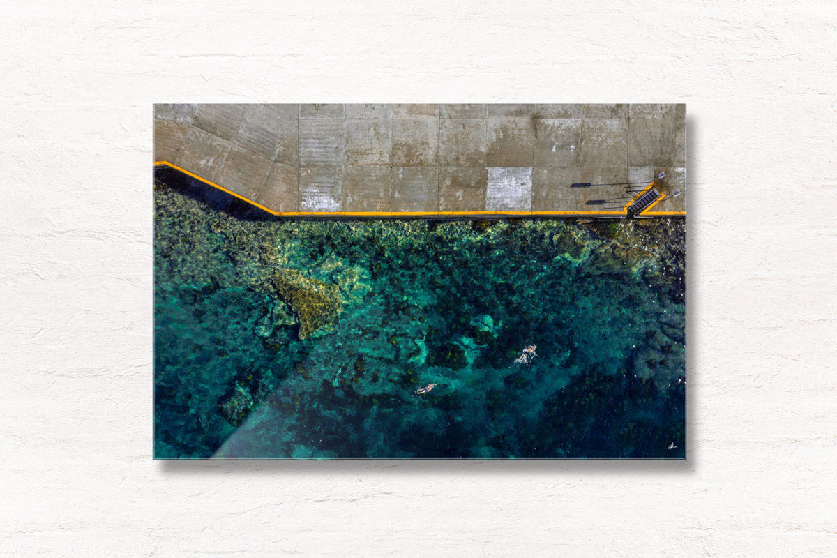 Long exposure of a swimmer stands on the edge of Bronte rockpool watching the sun rise over the horizon.