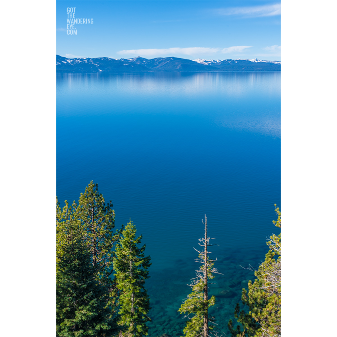 Aerial landscape above the pine trees and turquoise waters of Lake Tahoe, with mountains in the distance