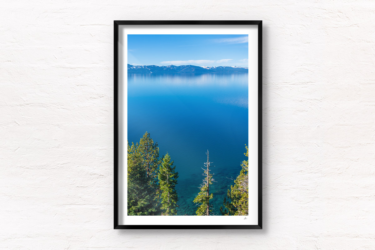 Aerial landscape above the pine trees and turquoise waters of Lake Tahoe, with mountains in the distance