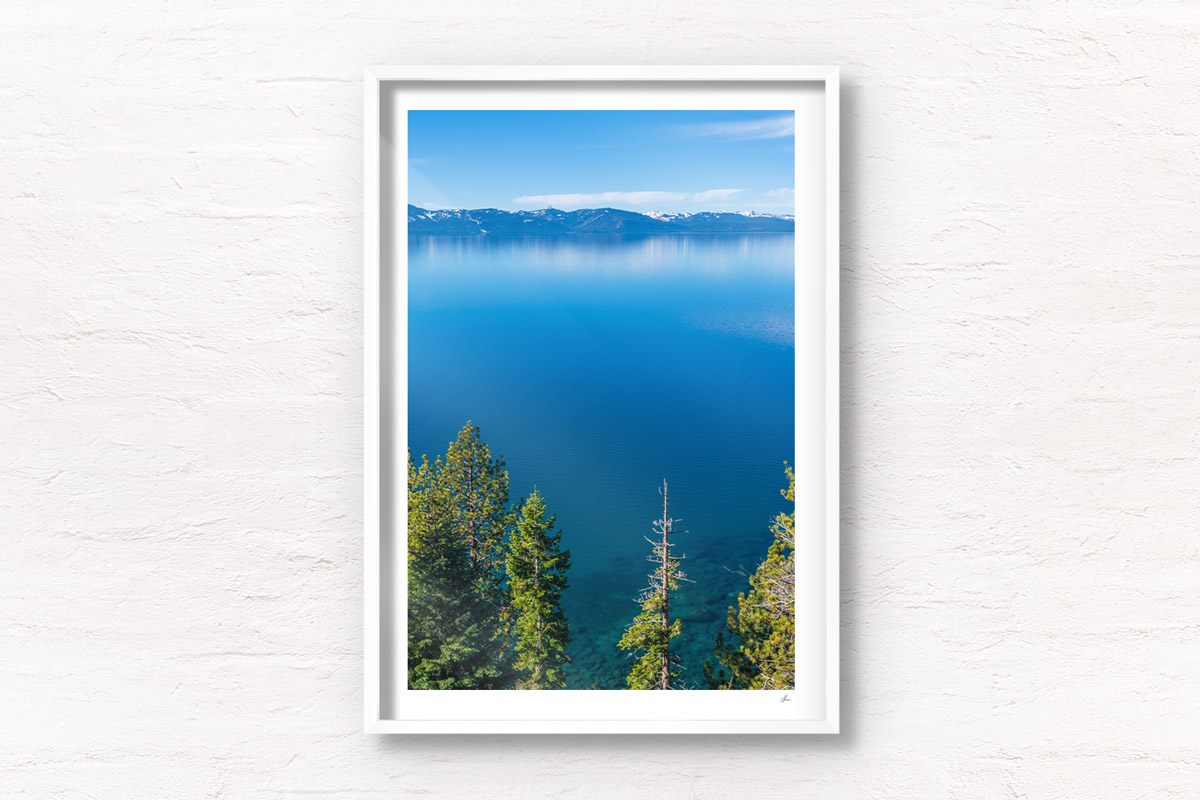 Aerial landscape above the pine trees and turquoise waters of Lake Tahoe, with mountains in the distance