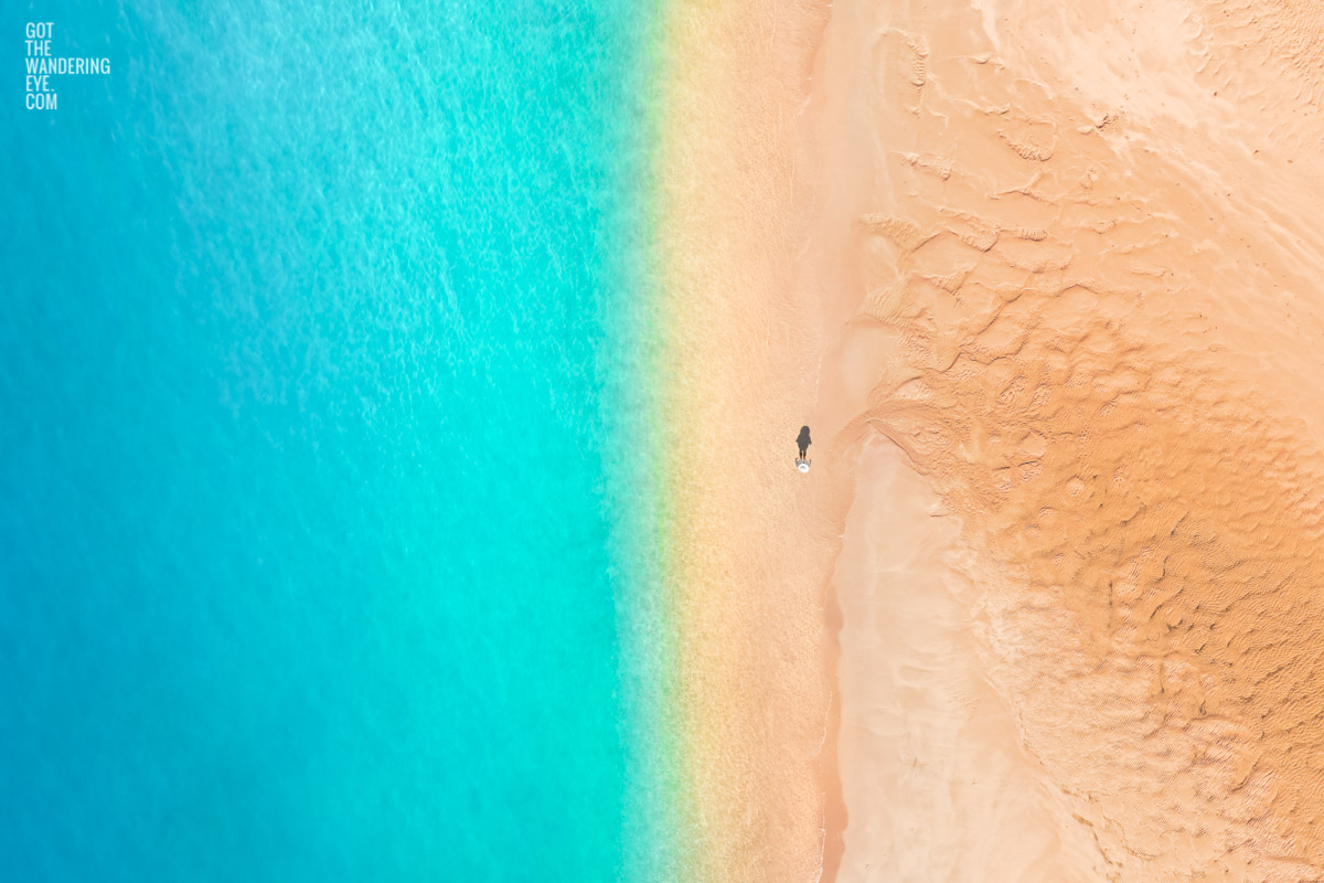 Aerial oceanscape above a woman walkign along deserted south coast beach