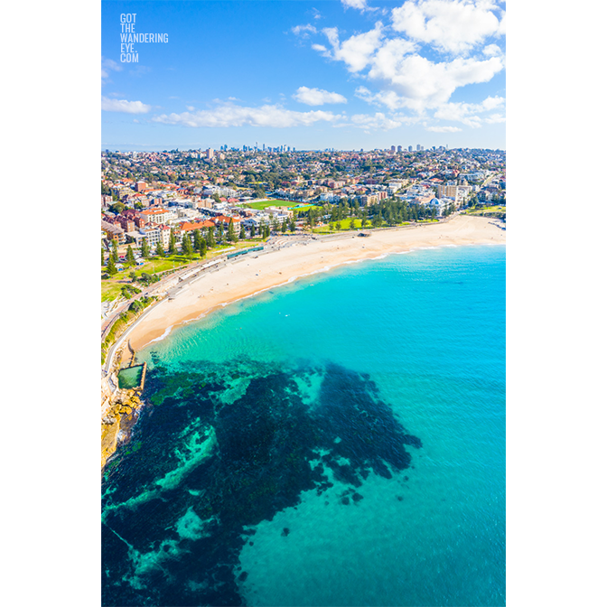 Aerial seascape above turquoise ocean waters of Coogee Beach looking back at the Sydney skyline in the horizon. Coogee Beach Aerial Landscape.