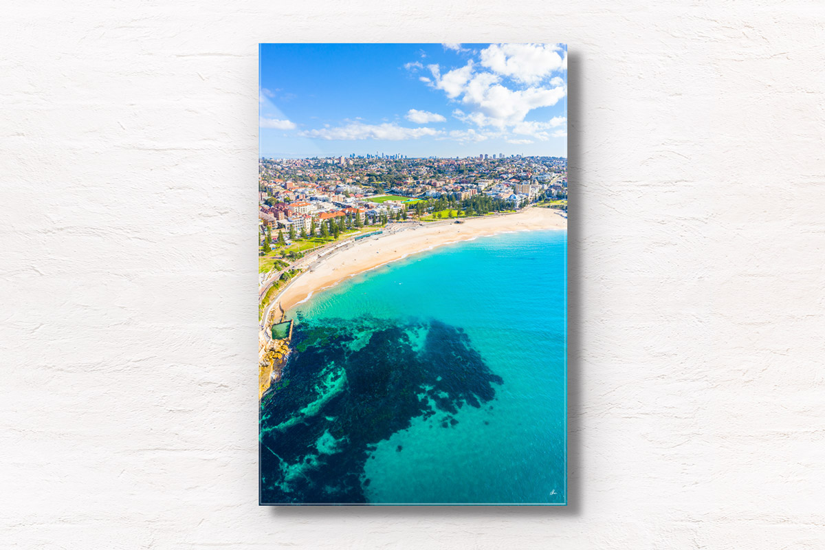 Aerial seascape above turquoise ocean waters of Coogee Beach looking back at the Sydney skyline in the horizon.