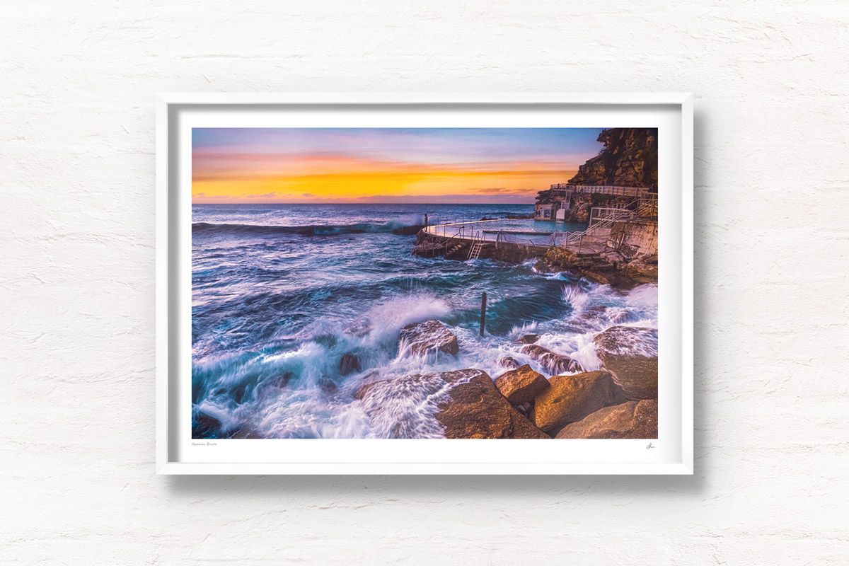 Long exposure of a swimmer stands on the edge of Bronte rockpool watching the sun rise over the horizon.