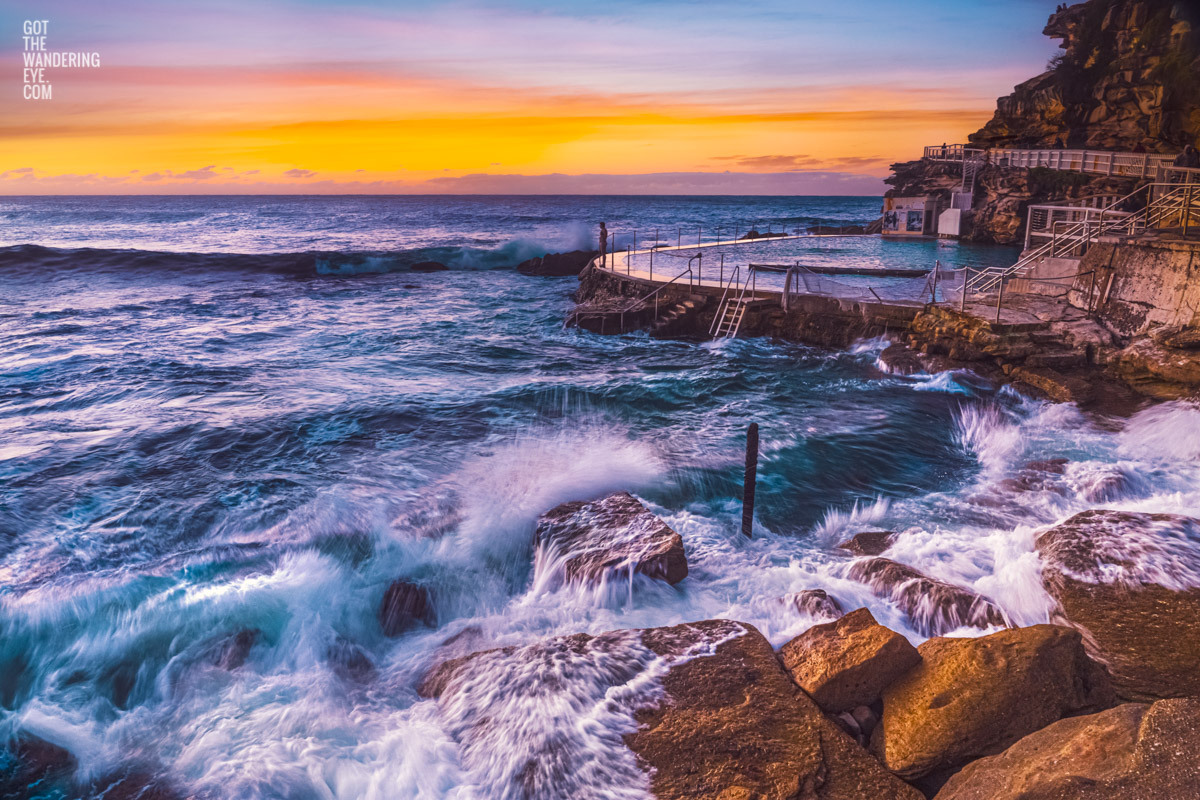 Long exposure of a swimmer stands on the edge of Bronte rockpool watching the sun rise over the horizon.