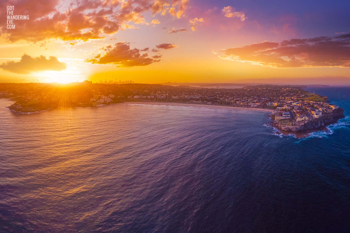 Aerial oceanscape above Bondi Beach looking back to a spectacular purple sky sunset setting on the Sydney skyline.