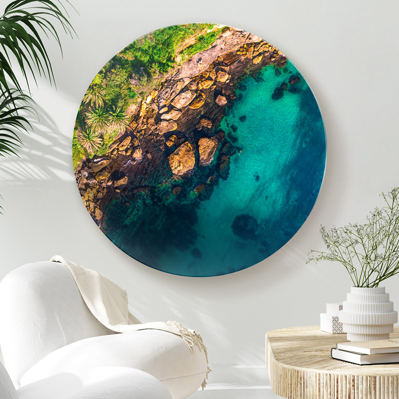 ChromaLuxe round metal wall art ocean prints. Aerial oceanscape above the tranquil calm waters of Gordons Bay. Tropical palm trees as a swimmer enjoys a swim. Wall art delivered and ready to hang.