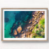 Framed wall art of man swimming in clear emerald waters of Gordons Bay, surrounded by palm trees and boulders from the clifftop.