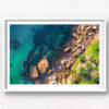 Framed wall art of man swimming in clear emerald waters of Gordons Bay, surrounded by palm trees and boulders from the clifftop.