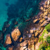 Man Swimming in clear emerald waters of Gordons Bay, surrounded by palm trees and boulders from the clifftop.