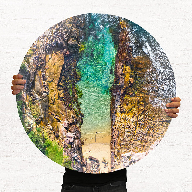 ChromaLuxe round metal print of the ocean. Aerial oceanscape above a woman enjoying a slither of the Sutherland Shires Cronulla Beach. Wall art delivered and ready to hang.