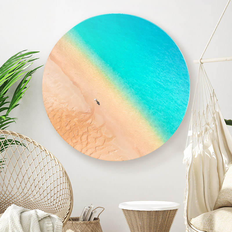 ChromaLuxe metal circle print of a woman standing on a deserted beach with turquoise coloured water, hanging in beachy home interior decor.