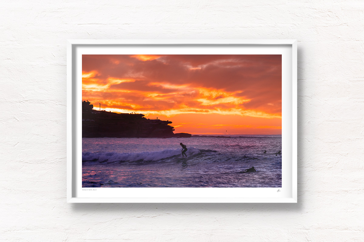 Surfer on a small wave with a scorching fiery sunrise over Ben Buckler at Bondi Beach