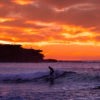 Surfer on a small wave with a scorching fiery sunrise over Ben Buckler at Bondi Beach