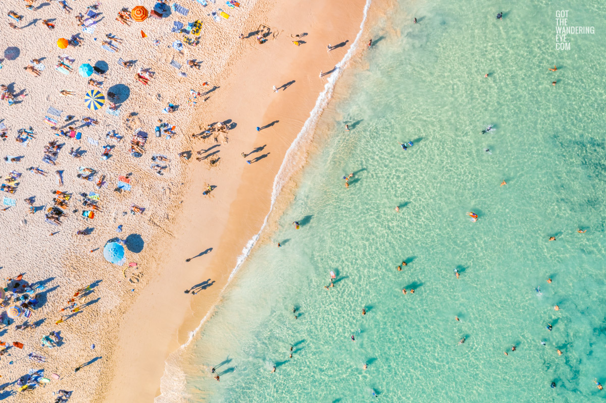 Swimmers and sunbathers enjoying a packed Bondi Beach with multi-coloured beach umbrellas on a Summers Day.