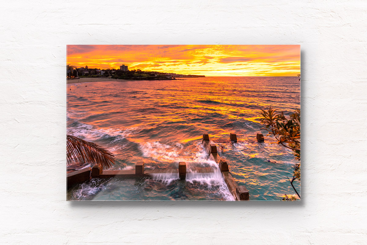 Swimmer enjoying a golden warm sunrise with waves crashing over the Ross Jones Memorial pool at Coogee