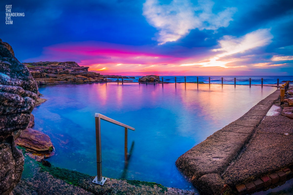 A pink sky cloudy sunrise over beautiful blue still waters and refections at an empty Mahon Pool, Maroubra.