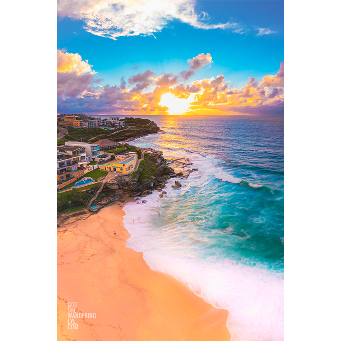 Golden sun rising over Tamarama Surf Life Saving Club, as swimmers enjoy a morning swim on an empty beach.