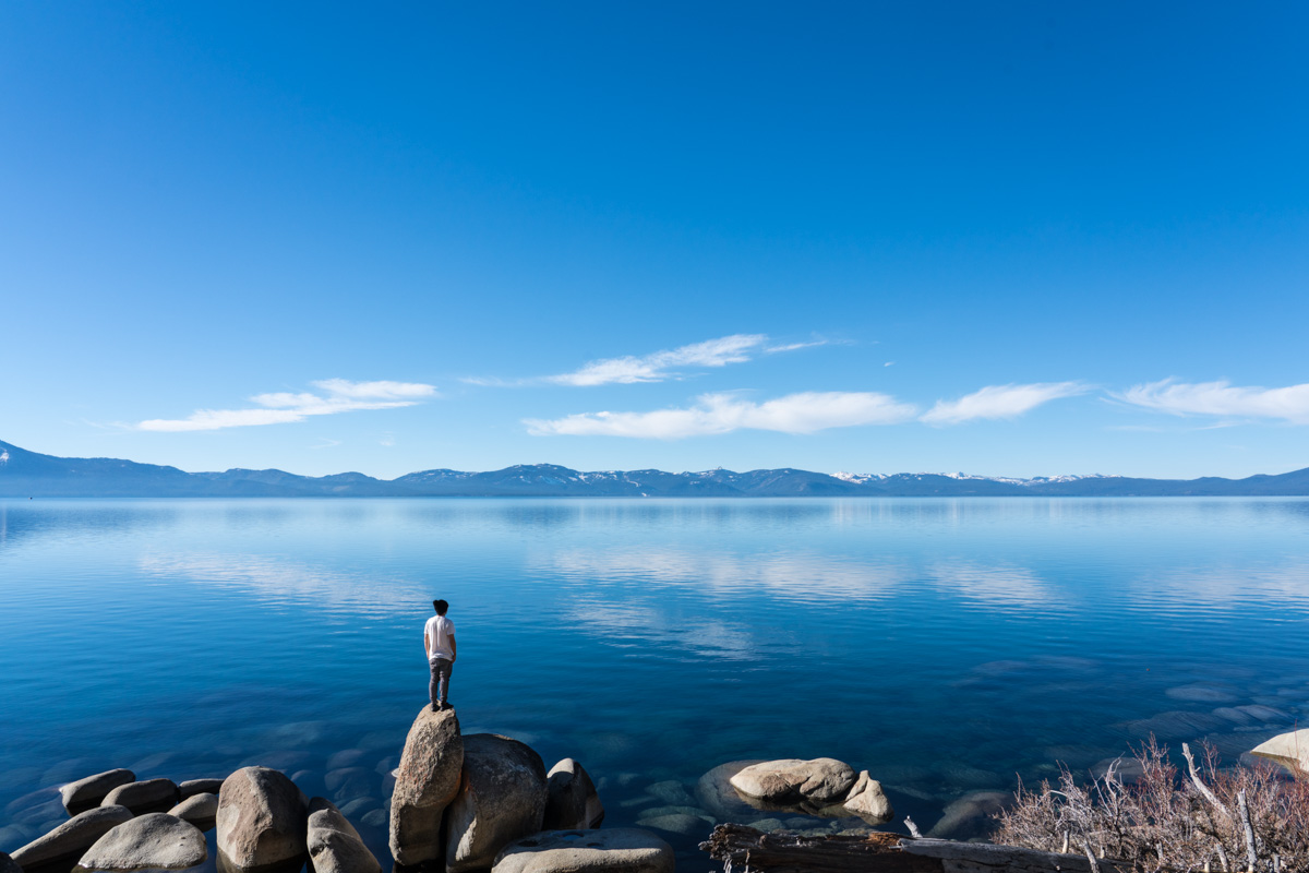 Travel photography by Allan Chan. Gotthewanderingeye standing on boulder, alone lakeside at Lake Tahoe, California.