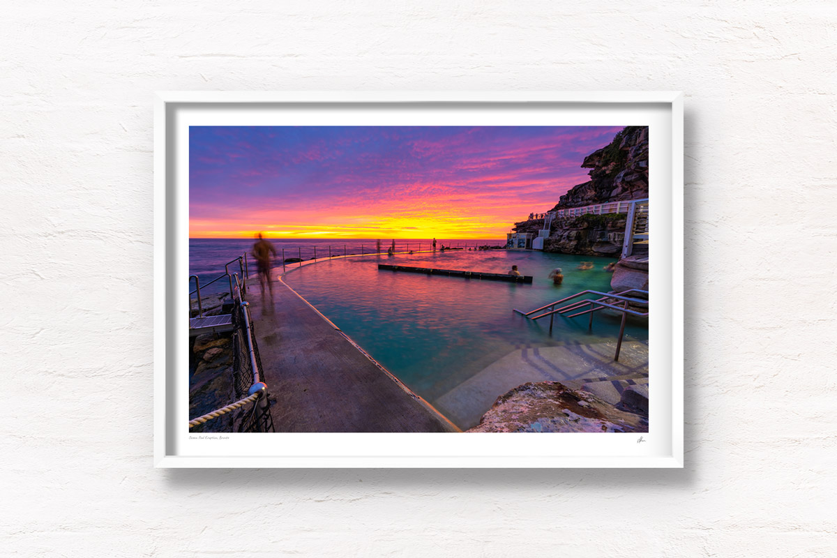 Spectacular fiery pink and yellow sun rise over swimmers enjoying a morning swim at iconic Bronte Ocean Pool Sydney.
