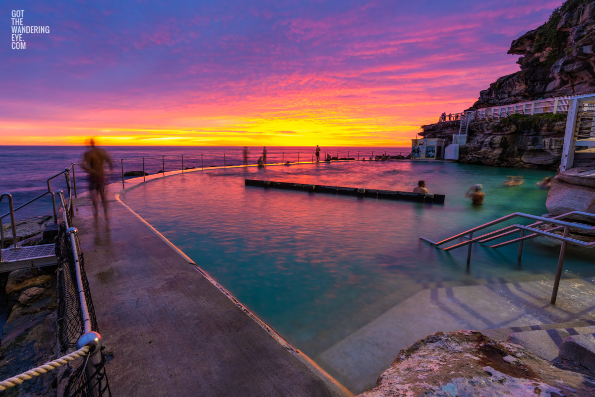 Spectacular fiery pink and yellow sun rise over swimmers enjoying a morning swim at iconic Bronte Ocean Pool Sydney.
