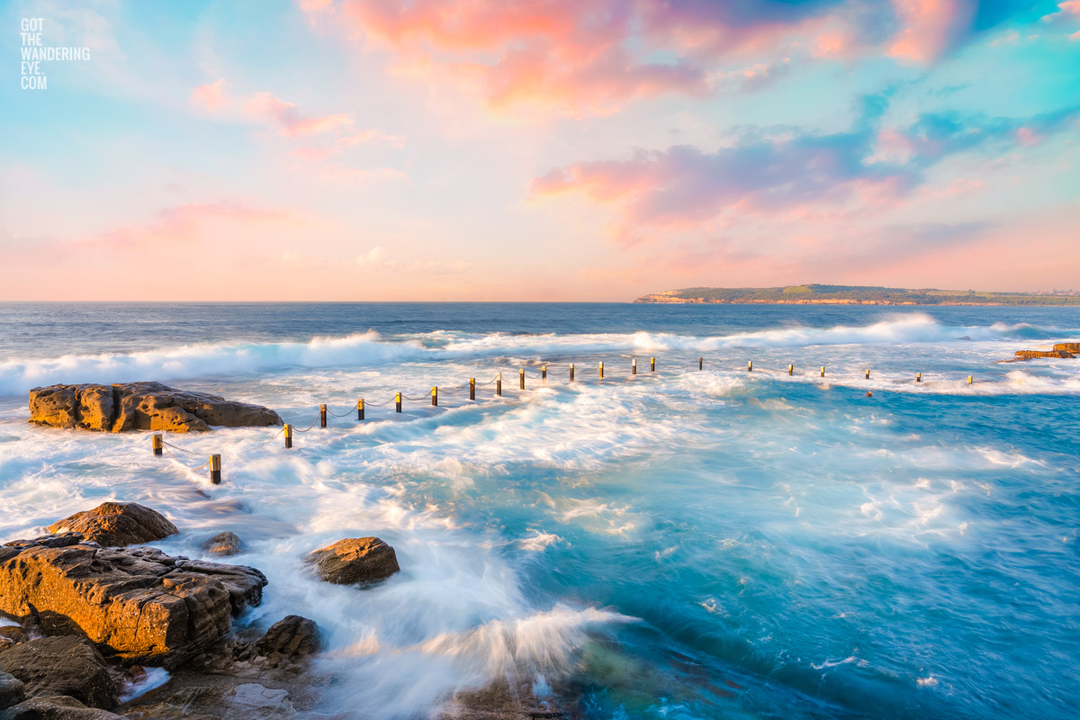 Mahon Pool Maroubra in Sydney getting smashed with waves on a dreamy sunset pink sky.