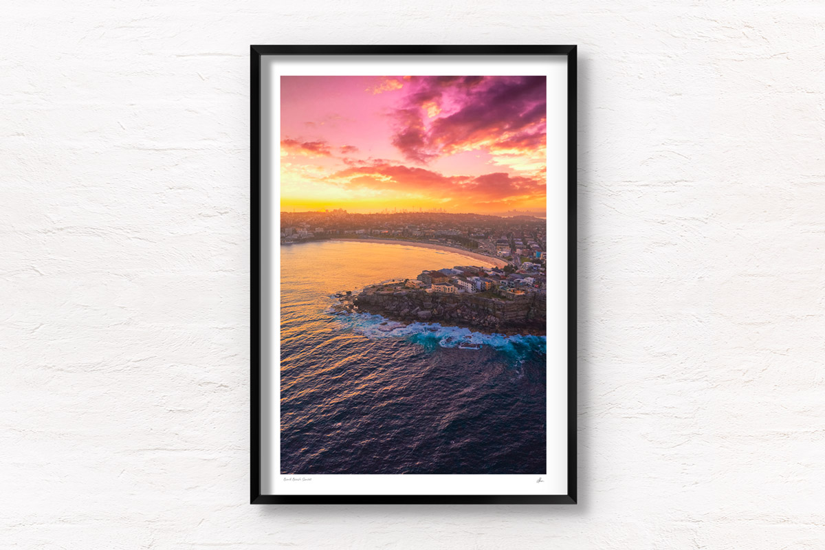 Aerial view above a Bondi Beach Sunset over the Sydney CBD skyline, glowing colour on the ocean waves.