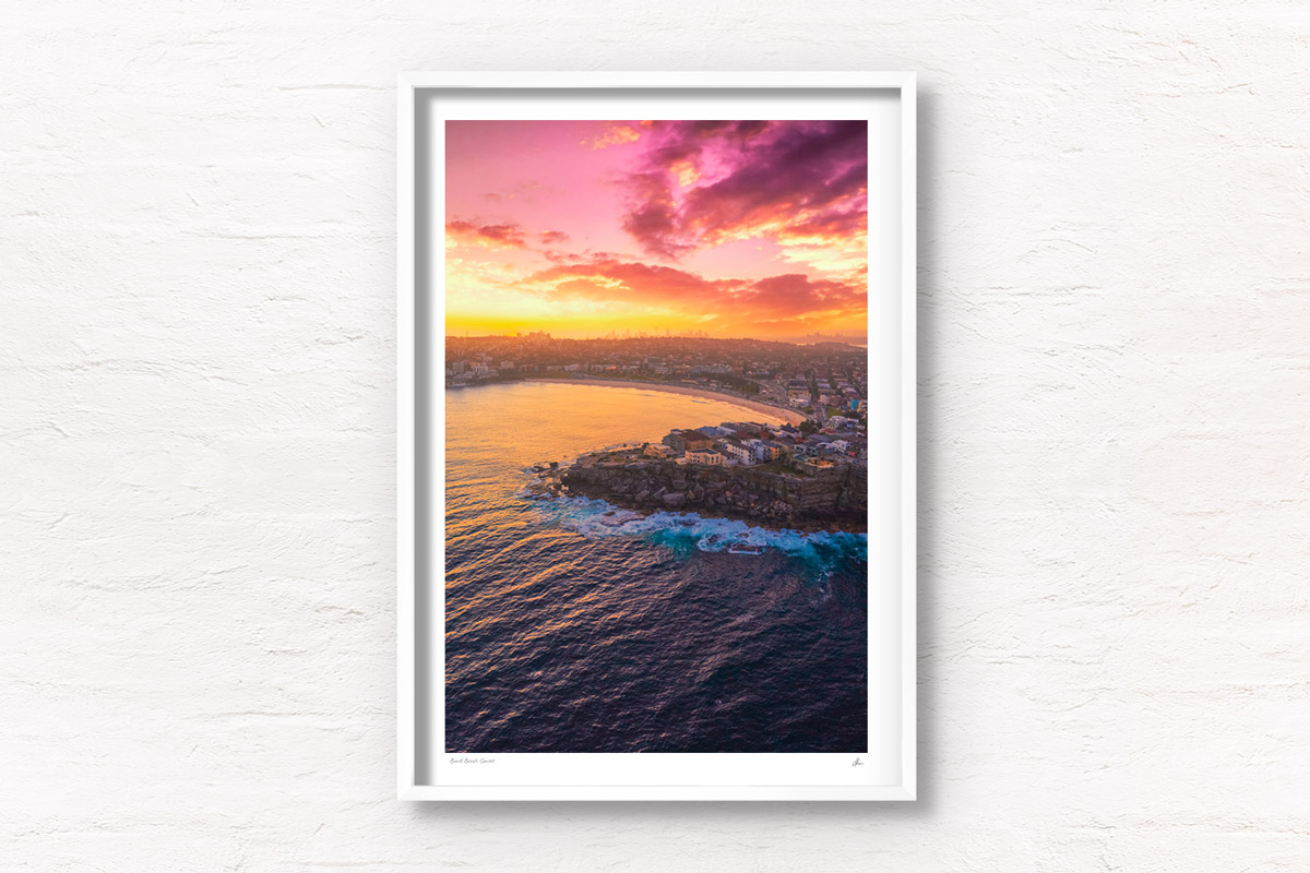 Aerial view above a Bondi Beach Sunset over the Sydney CBD skyline, glowing colour on the ocean waves.