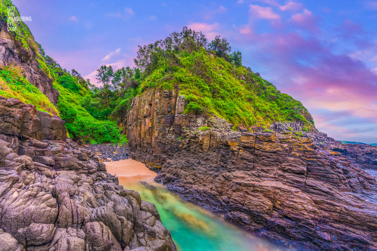 Tiny beach in between volcanic rock formation at the base of the Cathedral Rocks Cave in Kiama Downs during a purple sky sunrise.