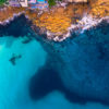 Aerial view above the blues of north Bondi Boat sheds and crystal clear ocean surrounding flat rock.