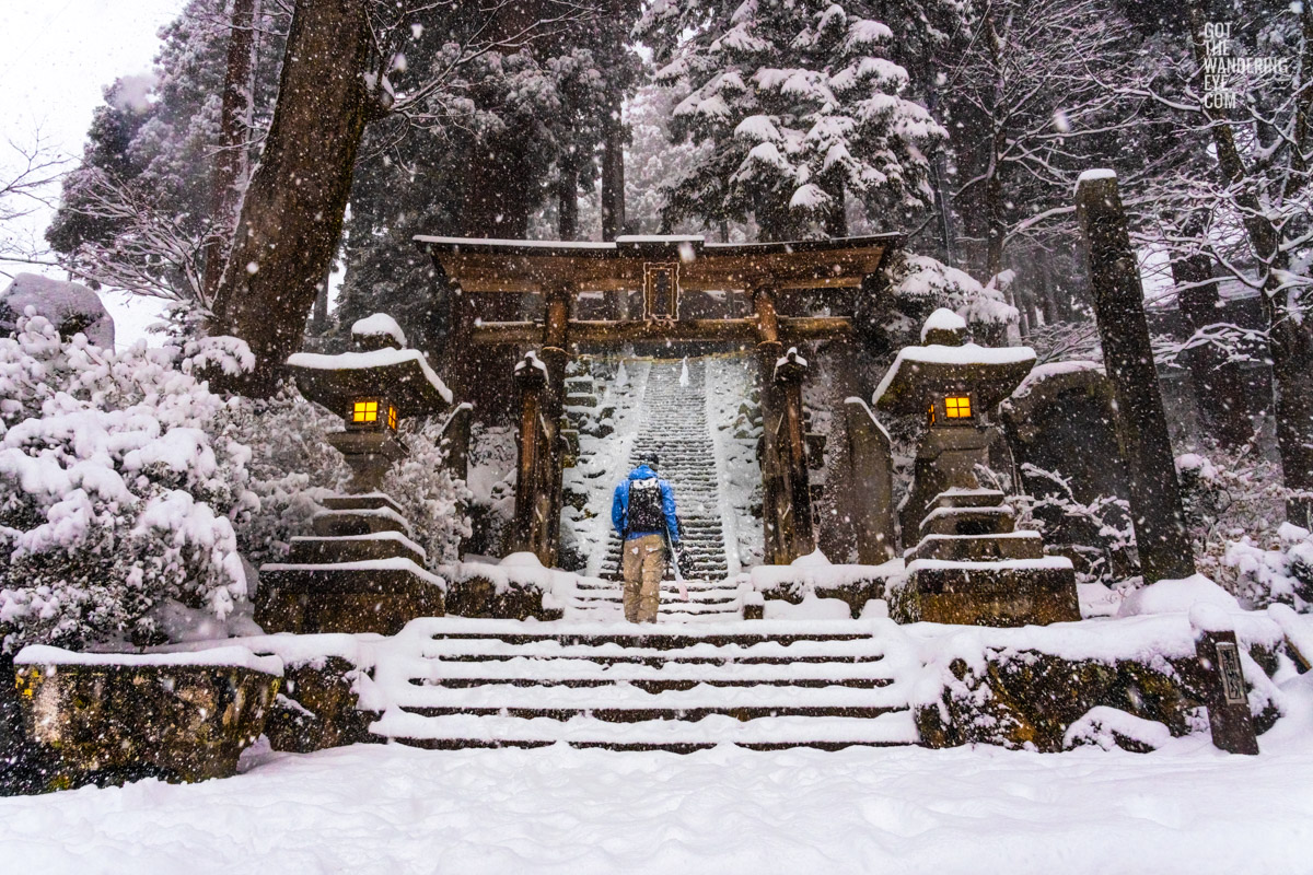 Snowboarder standing at the foot of the steps at Yuzawa Shrine praying for more snow covering the steps and shrine in Nozawa Onsen.