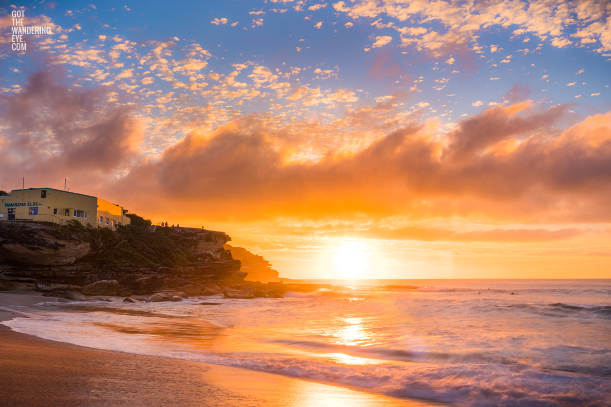 A glorious glowing sunrise through puffy clouds rising over Tamarama Beach