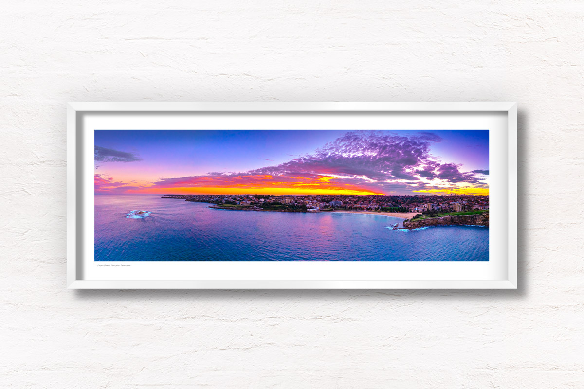 Aerial view above the ocean looking back at a Coogee Beach Sunset. Golden light through clouds with the Sydney CBD skyline on the horizon. Framed art photography wall art print.